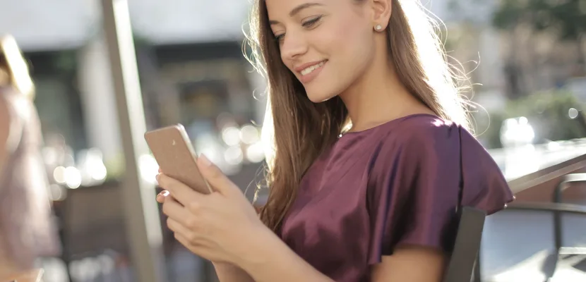 A woman checking a dating app on her phone at an outdoor cafe table