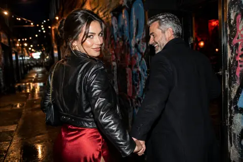 Illustrative image: a young woman in a red dress leading a laughing grey-bearded man down a Melbourne laneway at night