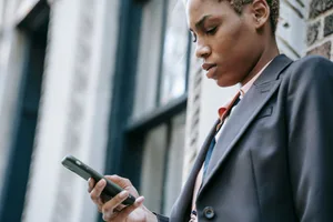 A woman in a blazer checking her phone outside an office building