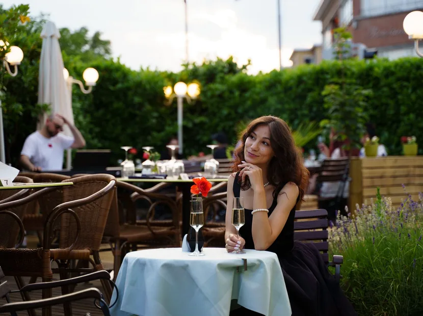 A woman in a black dress enjoying champagne alone at an outdoor restaurant terrace in the evening