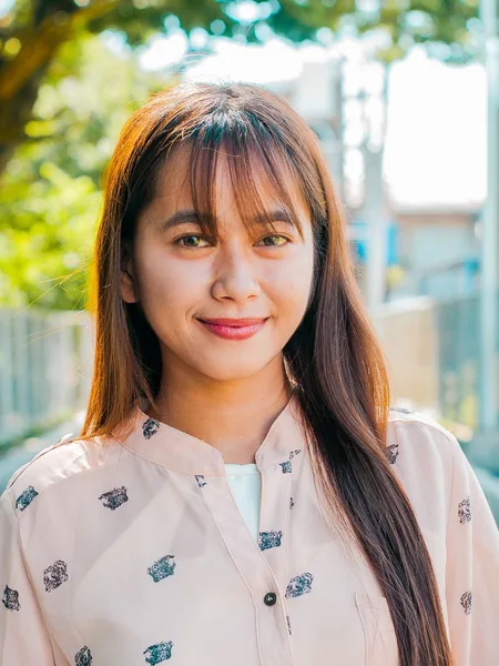 A confident young woman in a smart-casual blouse smiling at the camera outdoors in daylight