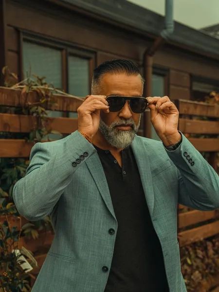 A distinguished grey-bearded man in a tailored suit outdoors
